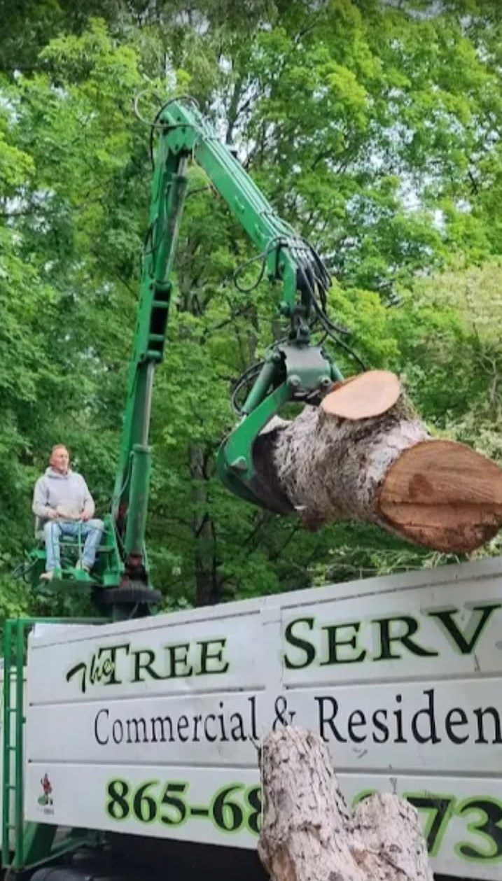 Knuckleboom crane lifting a cut trunk section over the truck bed